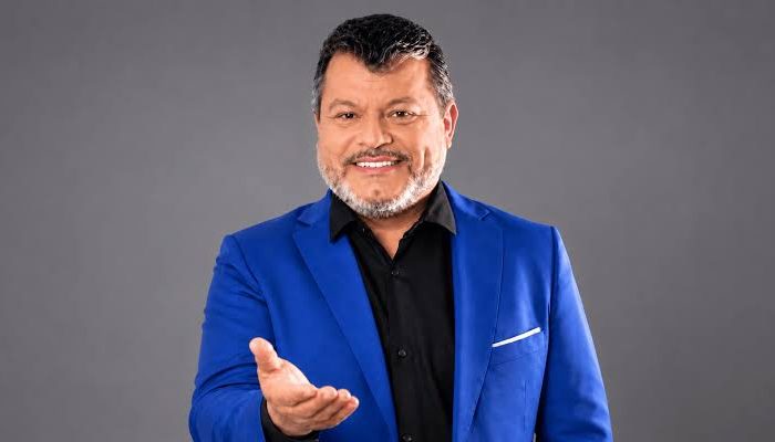 etrato do candidato Carlos Bernardo sorrindo com paletó escuro e camisa clara.
